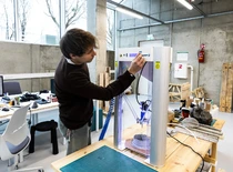 Studentas KTU „D-Lab“ laboratorijoje dirba su 3D spausdinimo įranga. Kūrybinė inžinerinė aplinka, skirta prototipų kūrimui ir eksperimentinei praktikai.