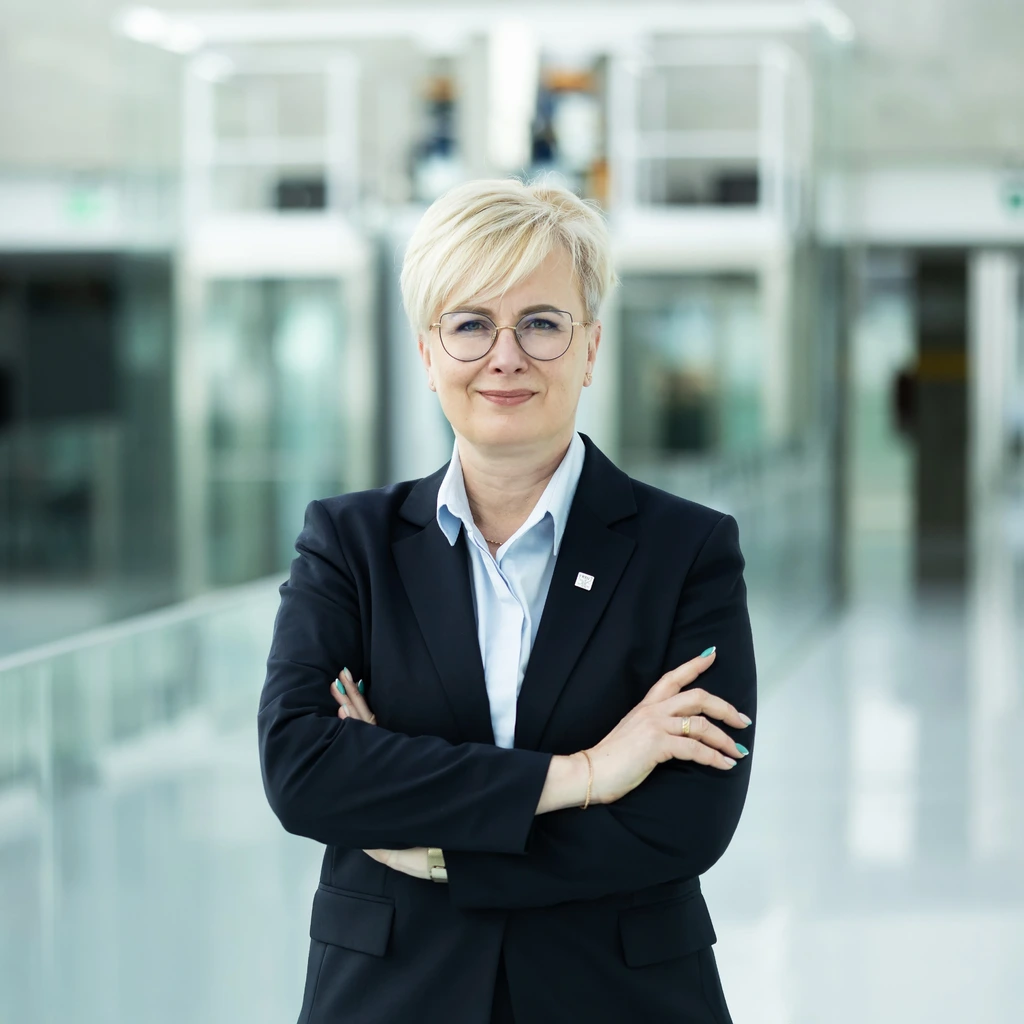 Jurgitos Stravinskienės, KTU Mokymosi visą gyvenimą centro vadovės, portretas Kauno technologijos universiteto „Santakos“ slėnio – mokslo, studijų ir verslo centro – interjero fone. Vidutinio amžiaus moteris trumpais šviesiais plaukais, dėvinti akinius, žvelgia tiesiai į kamerą su lengva šypsena. Stovi sukryžiavusi rankas, vilki klasikiniu tamsiu švarku ir žydros spalvos marškiniais.