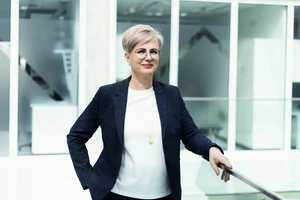 Doc. dr. Jurgita Stravinskienė, pasitikinti savimi, stovi šviesiame KTU "Slėnio" koridoriuje, vilkinti tamsiu švarku.