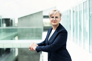 Jurgita Stravinskienė, KTU MVG centro vadovė, atsirėmusi į turėklą, šypsosi kamerai. Fone – šiuolaikiškas mokslo centro interjeras.